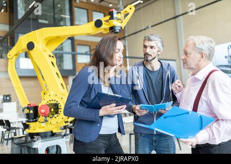 Engineers in factory having meeting in front of industrial robot Stock Photo