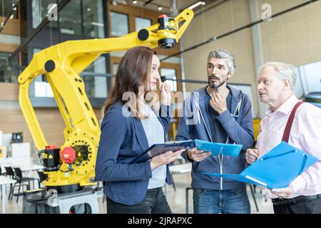 Engineers in factory having meeting in front of industrial robot Stock Photo