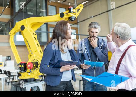 Engineers in factory having meeting in front of industrial robot Stock Photo