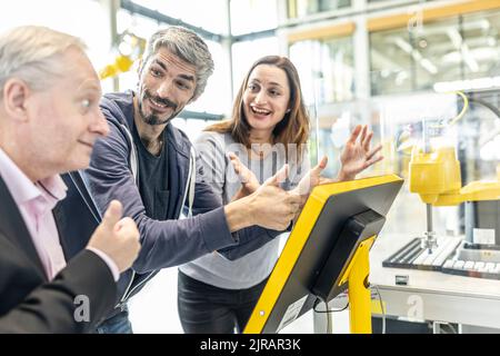 Happy colleagues giving thumbs up in robotic factory Stock Photo