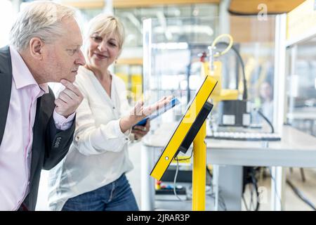 Smiling coworker presenting digital control to senior manager Stock Photo