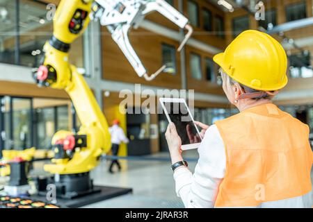 Skilled worker controlling robot arm with digital tablet Stock Photo