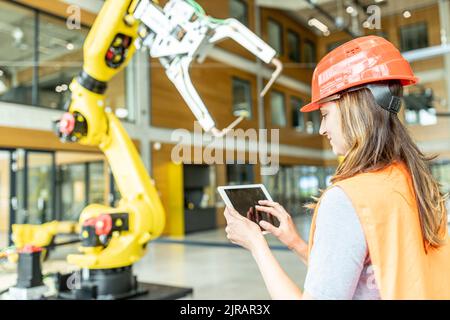 Skilled worker controlling robot arm with digital tablet Stock Photo