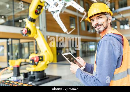 Confident skilled worker controlling robot arm with digital tablet Stock Photo