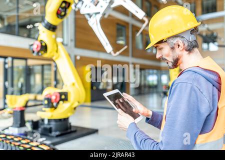 Skilled worker controlling robot arm with digital tablet Stock Photo
