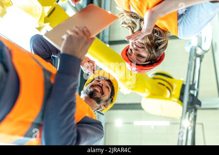 Male and female colleagues discussing robotic machine in industrial factory, low angle view Stock Photo