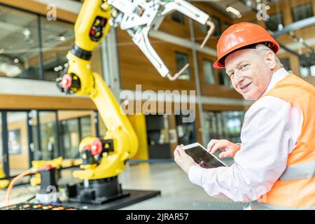 Confident skilled worker controlling robot arm with digital tablet Stock Photo