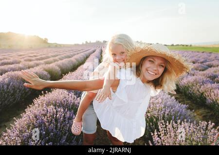 Happy woman giving piggyback ride to daughter in lavender field Stock Photo