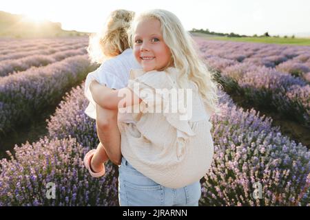 Woman giving piggyback ride to daughter in lavender field Stock Photo