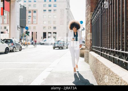Smiling businesswoman using smart phone walking in city Stock Photo