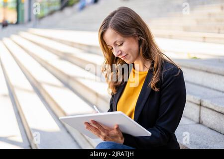 Smiling businesswoman using tablet PC sitting on steps Stock Photo