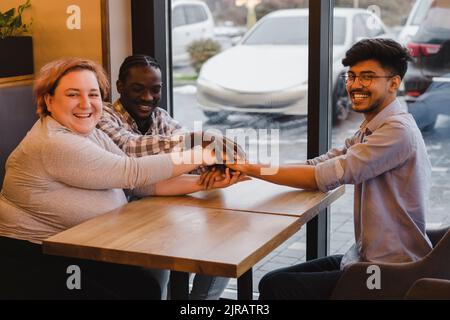 Happy multiracial friends stacking hands at table in cafe Stock Photo