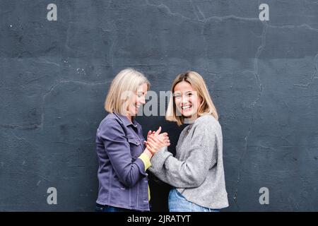 Happy mother and daughter holding hands by wall Stock Photo