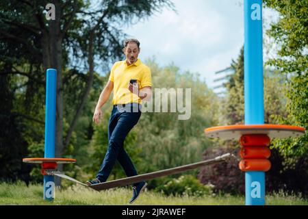 Surprised man looking at smart phone balancing on tightrope in park Stock Photo