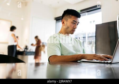 Young man using laptop sitting at table in cafe Stock Photo