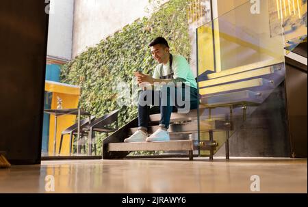Smiling young man text messaging through smart phone sitting on steps Stock Photo