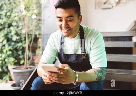 Happy man using mobile phone sitting on steps in coffee shop Stock Photo