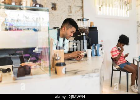 Man using mobile phone leaning on checkout in coffee shop Stock Photo