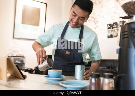 Happy young man wearing apron preparing coffee in cafe Stock Photo
