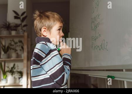 Thoughtful boy looking at spellings on whiteboard in home Stock Photo