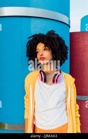 Young woman with curly hair in front of blue pipe Stock Photo