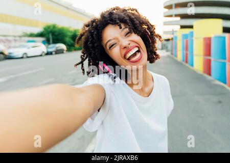 Cheerful young woman with curly hair taking selfie Stock Photo