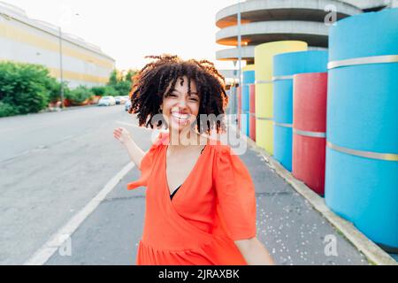 Happy woman with curly hair dancing on footpath Stock Photo