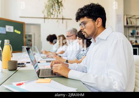 Young businessman working on laptop with colleagues at office Stock Photo
