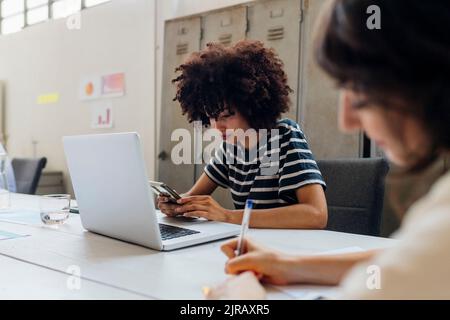 Businesswoman with laptop using smart phone at office Stock Photo