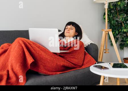 Woman lying on sofa using laptop at home Stock Photo