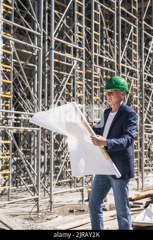 Architect examining blueprints standing in front of scaffolding Stock Photo