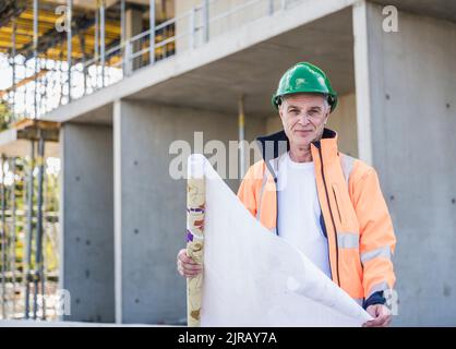 Smiling senior construction worker with blueprint at site Stock Photo