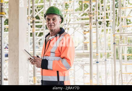 Senior contractor holding tablet PC standing in front of scaffolding Stock Photo
