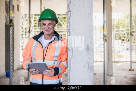 Smiling contractor with tablet PC leaning on column Stock Photo