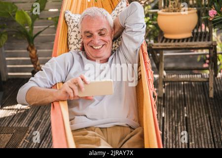 Happy retired man using phone in hammock Stock Photo