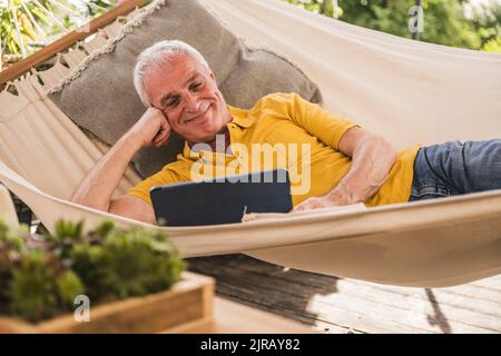 Smiling man using tablet PC lying in hammock Stock Photo