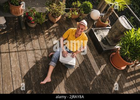 Happy man using laptop sitting on terrace Stock Photo
