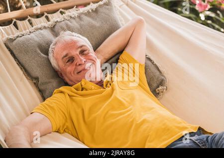Smiling retired senior man with hand behind head relaxing in hammock Stock Photo