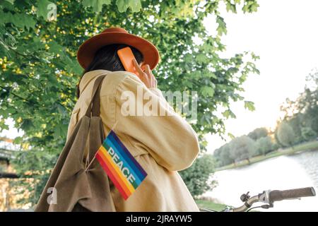 Woman talking on smart phone with peace flag hanging from bag Stock Photo