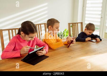 Happy girl using tablet PC sitting by brothers with technologies at home Stock Photo