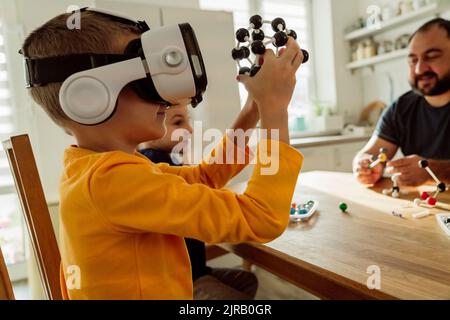 Boy wearing virtual reality goggles examining molecules at home Stock Photo