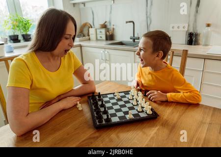 Mother and son playing chess in kitchen at home Stock Photo