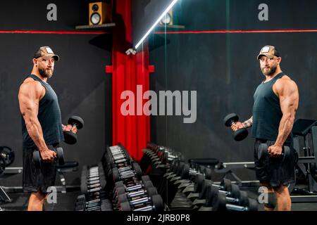 Bodybuilder exercising with dumbbells standing in gym Stock Photo