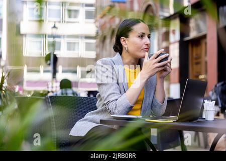 Thoughtful businesswoman holding coffee cup at sidewalk cafe Stock Photo