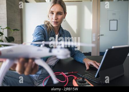 Woman examining drone using tablet PC at office Stock Photo