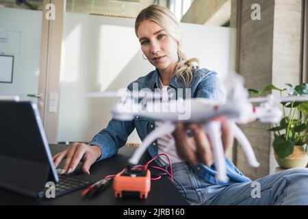 Blond woman holding drone using tablet PC in office Stock Photo
