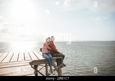 Mature couple sitting on jetty over sea Stock Photo