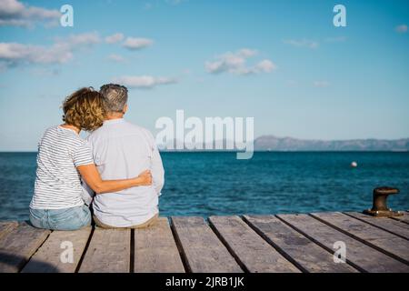 Mature couple spending time together sitting on jetty looking at sea Stock Photo