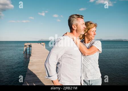 Smiling woman with man standing at jetty in front of sea Stock Photo