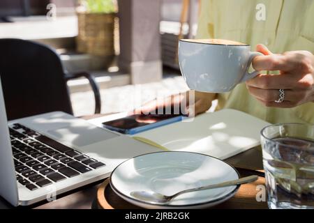 Hand of freelancer holding coffee cup at sidewalk cafe Stock Photo